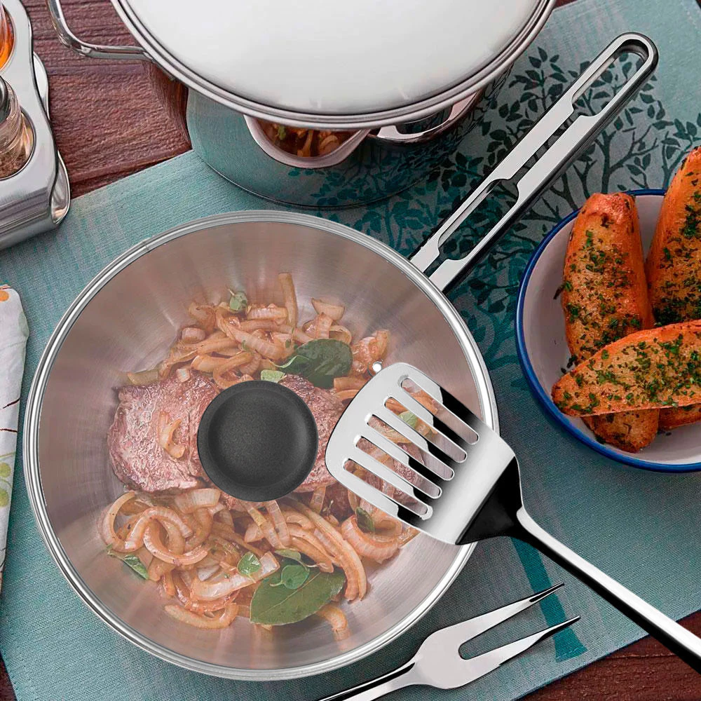 Frigideira Alegra de aço inox prateada, com fundo triplo visível, sobre um fogão de indução, selando um pedaço de carne com perfeição.