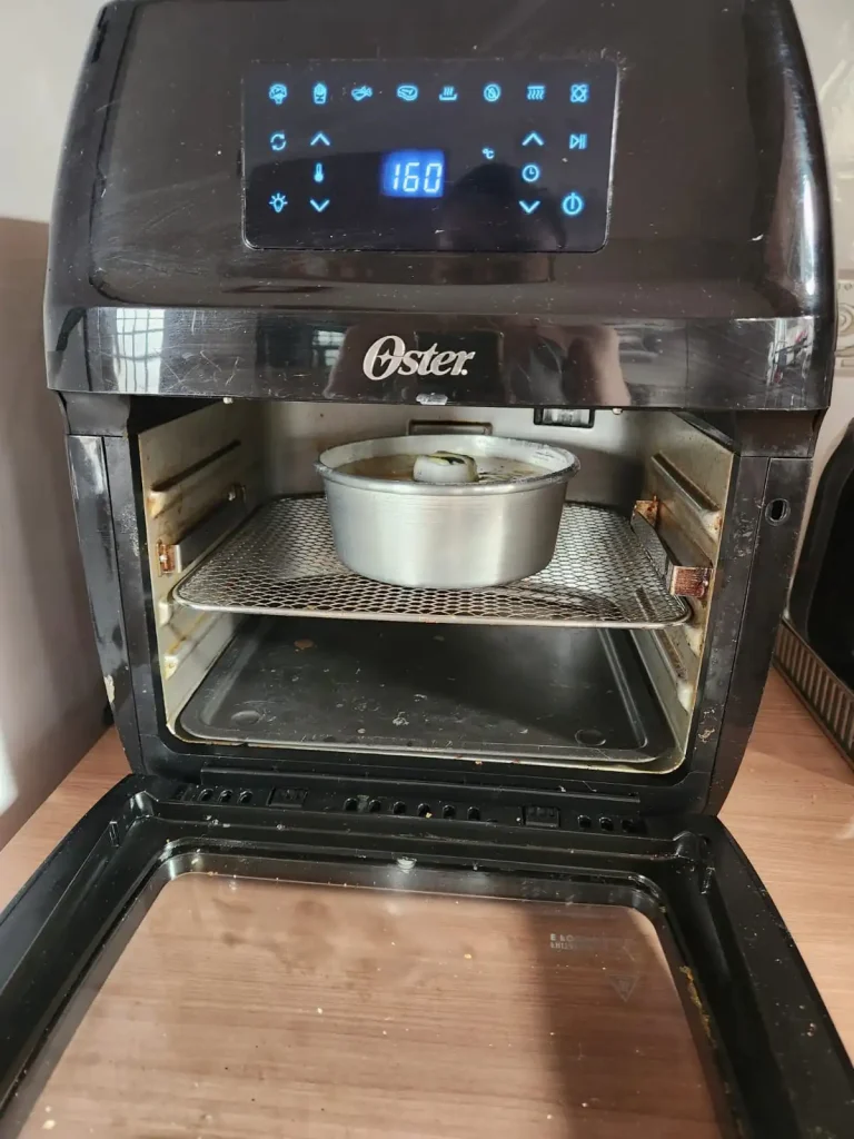 Forma de alumínio com massa de bolo dentro de uma air fryer Oster ligada a 160 graus.