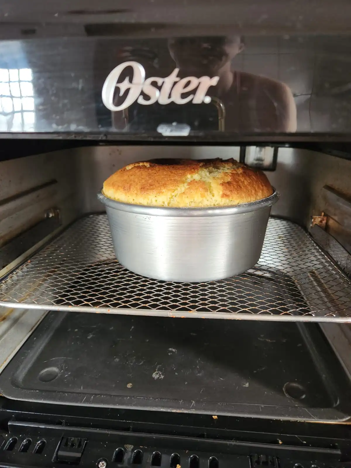 Bolo caseiro dourado assando em forma de alumínio dentro de uma air fryer Oster.