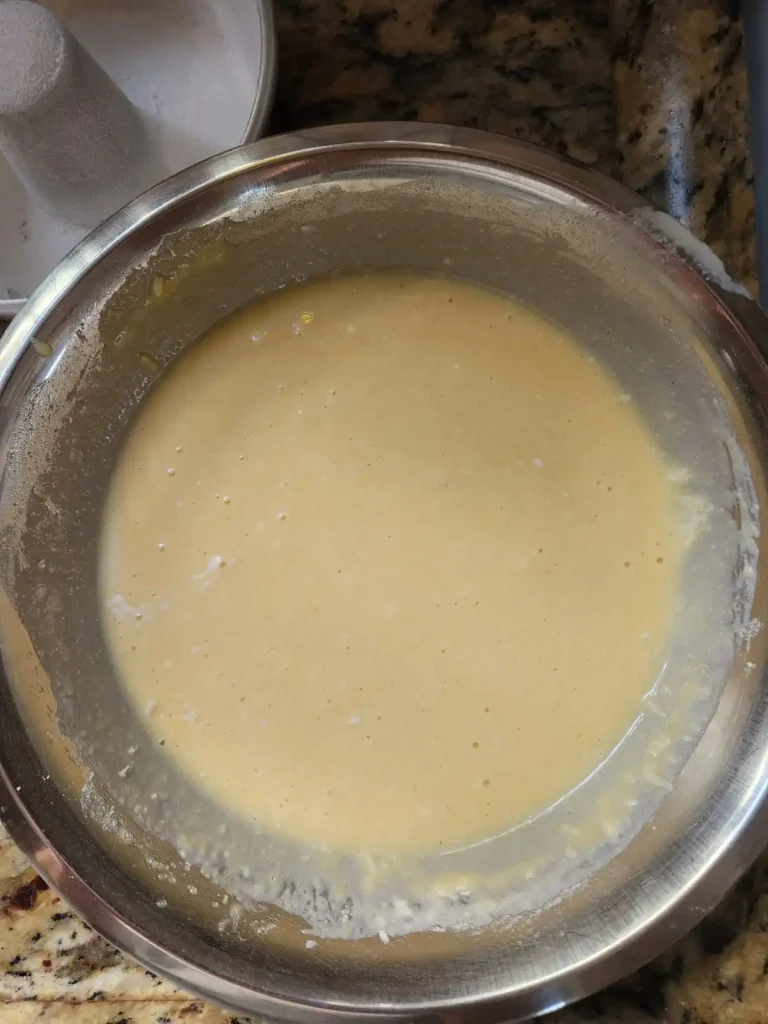 Tigela de inox com massa de bolo cremosa e homogênea sobre bancada de granito na cozinha.