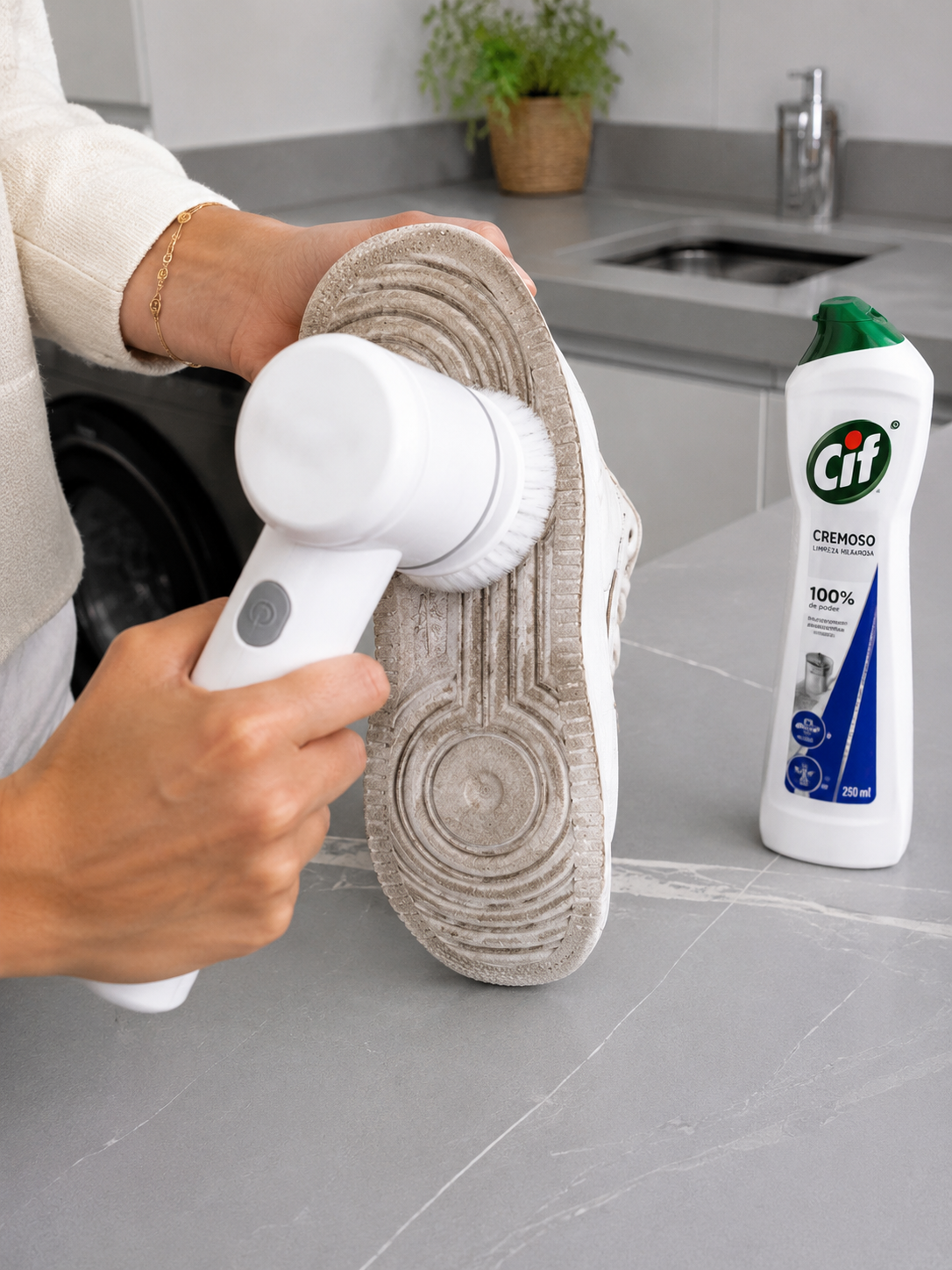 Escova elétrica sem fio sendo usada para limpar a sola de borracha de um tênis branco com o produto CIF cremoso ao lado.